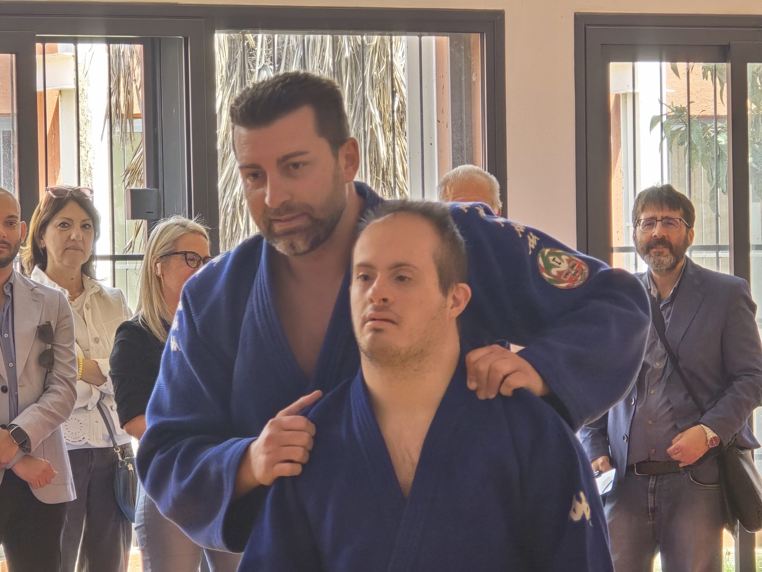 maestro di judo e ragazzo si preparano per una dimostrazione in presenza di alcuni spettatori; indossano un Judogi blu